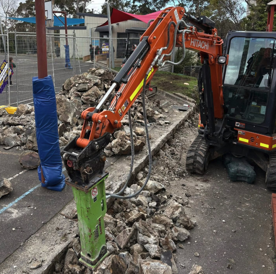 EROC Hitachi excavator with rock breaker working within an operating school